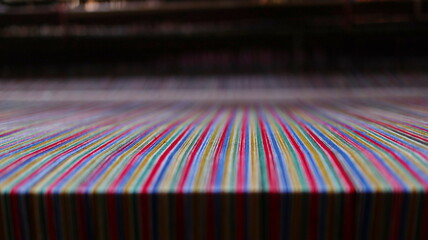 Colorful threads being woven on a loom in a textile factory, creating a vibrant striped pattern, showcasing the intricate process of fabric production.