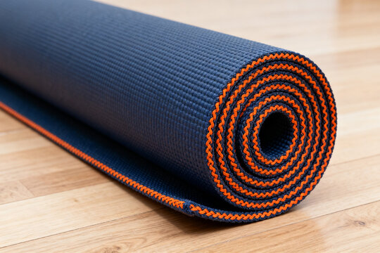 Rolled blue yoga mat with orange trim on wooden floor