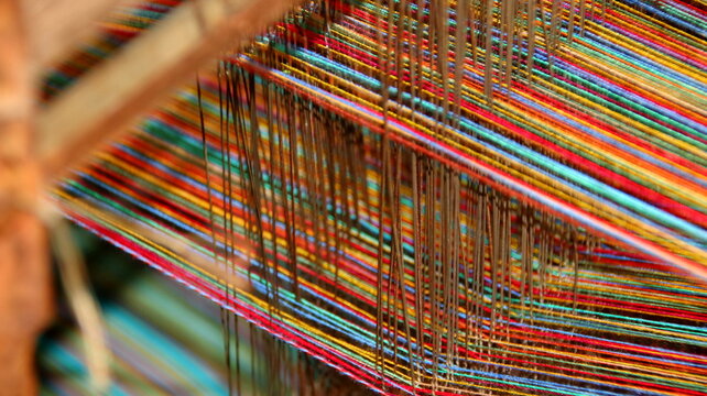 Colorful threads stretch tautly across a wooden loom in a textile workshop, showcasing the intricate process of weaving with vibrant hues and textures.