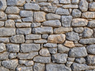 Obraz premium A background of a rustic dry-stack stone wall. Weathered grey and brown rocks form a solid, ancient pattern.