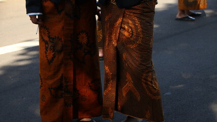 People wearing traditional batik sarongs walk on city street during cultural festival, showcasing intricate patterns and vibrant colors in a celebration of heritage. © onyengradar