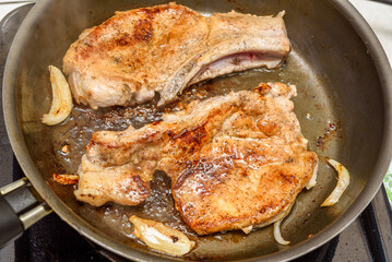 Fried meat on the bone with onions in a hot frying pan.