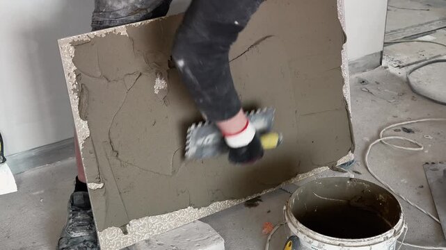 A master tiler applies glue to large-format tiles with a spatula