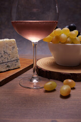 Taglieri con formaggio e uva, calice di vino rosè in primo piano