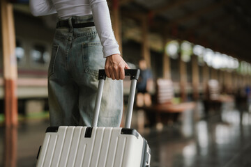 Stylish young woman traveling at train station with suitcase, traveling alone on vacation or business trip, enjoying summer city adventure.