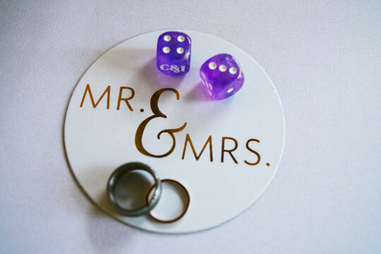 Two wedding rings and two purple dice on a circular coaster that reads Mr. and Mrs.