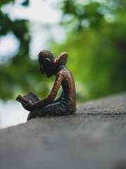 Miniature statue of Dracula reading a book, one of Mihály Kolodko’s artworks in Budapest, located near Vajdahunyad Castle, with fine bronze details and surrounded by greenery.