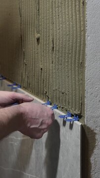 a master tiler pushes a tile leveling system under the tile