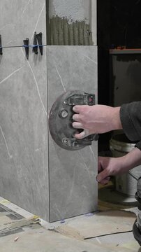 Master tiler installs gray tiles on the wall with special suction cups