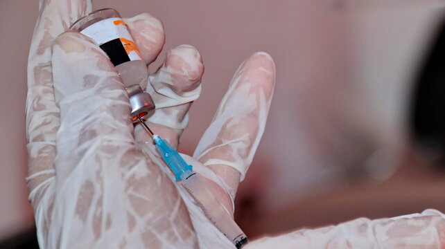 Healthcare worker prepares vaccine dose by drawing liquid into syringe in hospital setting, highlighting medical procedure and focus on patient care. - Powered by Adobe