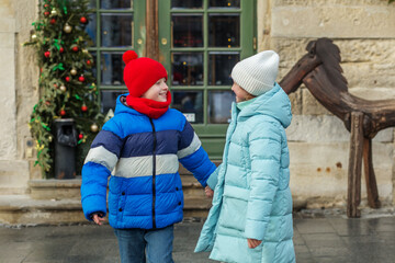 Happy kids in winter coats holding hands outdoors. Holiday season. © Olha Tsiplyar