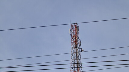 Tall cell tower transmitting signals against a clear blue sky with power lines in the foreground,...