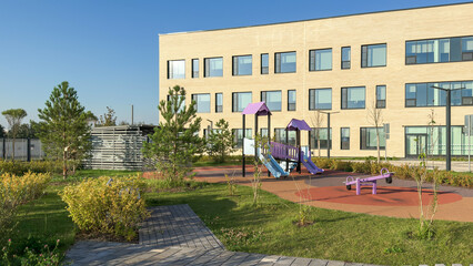 Modern kindergarten school territory with outdoor playground, colorful slides, swings, landscaped greenery, rubber. Concept of child care, preschool, elementary education, and urban infrastructure.