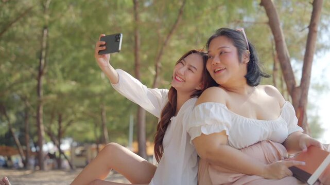 Happy Asian woman using mobile phone during travel nature the sea on summer beach holiday vacation. Women friends enjoy and fun outdoor lifestyle using smartphone taking selfie together at the beach.