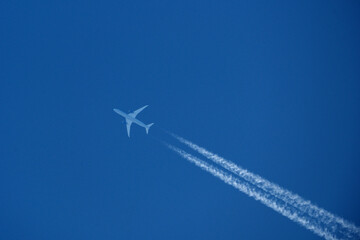 Airplane in the blue sky with contrail, closeup of photo. Airplane in the blue sky with white trace of a plane.