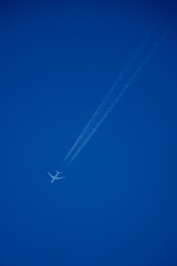 Airplane in the blue sky with contrail, closeup of photo. Airplane in the blue sky with white trace of a plane.