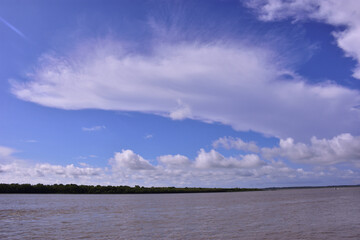 Obraz premium Scenic wide-angle view of the Bakkhali River in Cox’s Bazar, Bangladesh, with flowing water under a dramatic blue sky filled with white clouds. A natural landscape of river and sky.