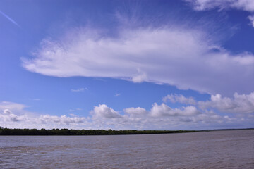 Obraz premium Scenic wide-angle view of the Bakkhali River in Cox’s Bazar, Bangladesh, with flowing water under a dramatic blue sky filled with white clouds. A natural landscape of river and sky.