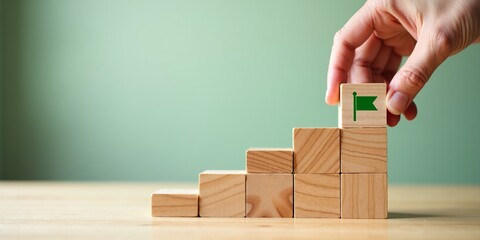 Business goal achievement, career growth, and success concept. Hand placing final wooden block with a flag on a staircase.