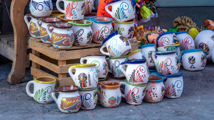 A collection of handcrafted ceramic cups with vibrant colors and intricate designs are displayed on...