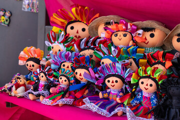 A group of dolls with various outfits and accessories are displayed on a pink surface. Historic center of Queretaro City, decorations and traditions to celebrate Mexico's Independence Day, colonial ar
