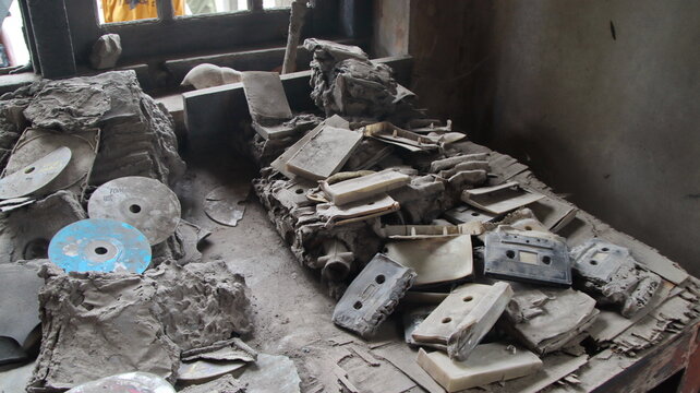 Dusty old cassettes and cds sit on a table in an abandoned building, showcasing forgotten technology and a sense of decay and neglect.