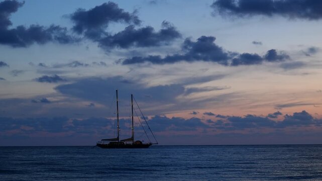 Oglaistro Marina, Italy. Blue hour seascape at Baia Arena, Ogliastro Marina Bay, Italy: calm Tyrrhenian waters and soft pastel clouds after sunset, with a two-masted sailing ship far on horizon. 4K.