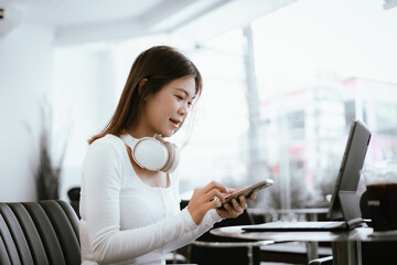 Obraz premium Smiling young woman with braces wearing headphones, working on laptop at cafe, enjoying online learning or remote work.