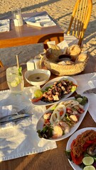 The image shows a table with seafood dishes, salad, bread, and drinks on a terrace overlooking the sea. The setting is perfect for a relaxing meal with a view of the beach and palm trees.