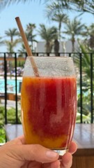 Two glasses of colorful drinks on a wooden table, surrounded by white sofas and palm trees, creating a relaxing outdoor atmosphere.