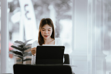 Fototapeta premium Young woman holding credit card and smartphone, making online payment while using laptop in modern cafe.