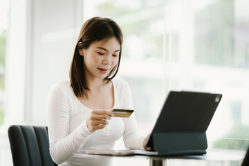 Young woman holding credit card and smartphone, making online payment while using laptop in modern cafe.