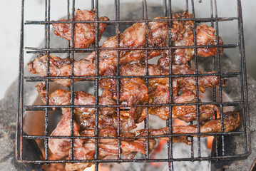 close-up shot of marinated meat grilling on a metal wire rack over an open flame or charcoal.