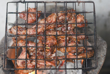 close-up shot of marinated meat grilling on a metal wire rack over an open flame or charcoal.