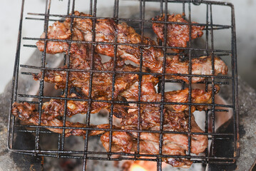 close-up shot of marinated meat grilling on a metal wire rack over an open flame or charcoal.