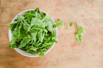 overhead shot focusing on a white bowl filled with fresh, bright green leaves placed on a light wooden surface.