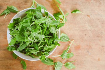 overhead shot focusing on a white bowl filled with fresh, bright green leaves placed on a light wooden surface.