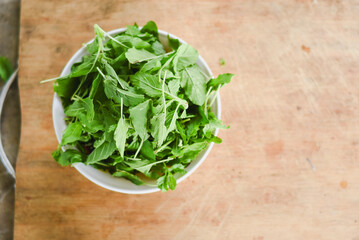 overhead shot focusing on a white bowl filled with fresh, bright green leaves placed on a light wooden surface.