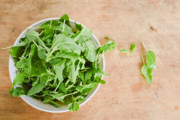 overhead shot focusing on a white bowl filled with fresh, bright green leaves placed on a light wooden surface.