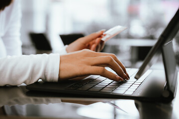 Close-up of woman holding credit card and typing on laptop, making online payment and shopping securely.