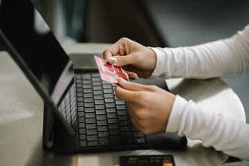 Close-up of woman holding credit card and typing on laptop, making online payment and shopping securely.