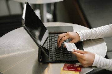 Close-up of woman holding credit card and typing on laptop, making online payment and shopping securely.