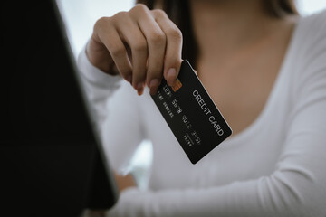 Close-up of woman holding credit card and typing on laptop, making online payment and shopping securely.