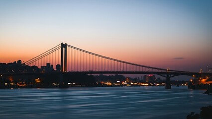 Fototapeta premium Silhouetted suspension bridge at dusk with city lights