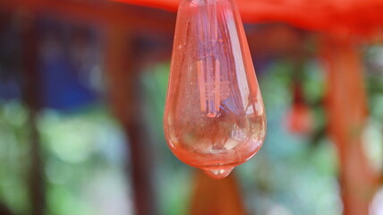 Closeup of a translucent red glass droplet hanging from a colorful structure in a whimsical outdoor setting, creating a sense of wonder and artistry.
