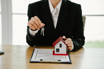 Businesswoman holding house keys with a model house on contract document, symbolizing real estate...