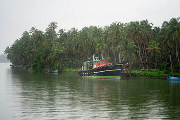 Naklejka premium blue deep water fishing boats with the poles and harnesses parked on a riverside jetty in the backwaters during a rain shower
