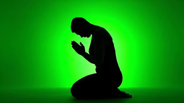Silhouette of Person Kneeling in Prayer on Green Background