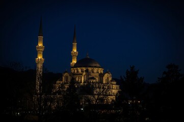 A beautifully illuminated mosque with two tall minarets stands against a deep blue evening sky, creating a serene and majestic silhouette.