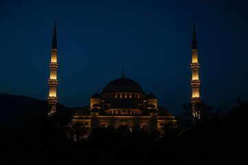 A beautifully illuminated mosque with two tall minarets stands against a deep blue evening sky, creating a serene and majestic silhouette.